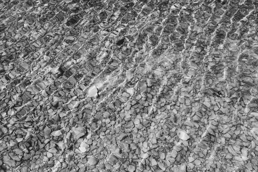 Stones under water. Sea pebbles on the beach. Sea pebbles on the beach sand with transparent water. Natural sea stones closeup. Beach smooth pebbles. Tourism and travel themed. Vacation background. 