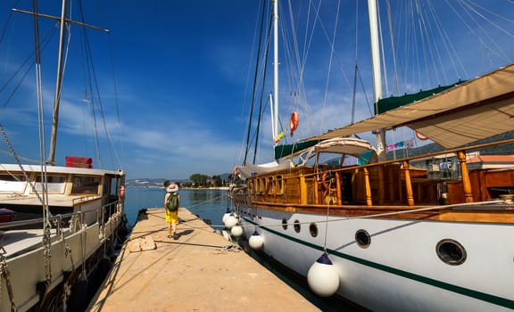 Docked ship in port. Docking on the pier in the Mediterranean. Yacht parked at dock. Tourist with backpack walking on the pier.

