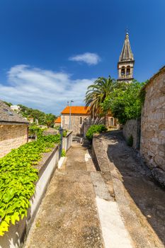 Church building and palm tree against sunny blue sky in Splitska village on Brac island, Croatia. 