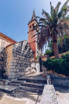 Church building and palm tree against sunny blue sky in Splitska village on Brac island, Croatia. 