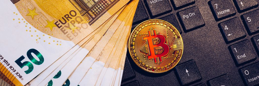 Golden bitcoin over Euro money. Bitcoin cryptocurrency. Crypto currency concept. Bitcoin with euro bills. Bitcoins stacked on euro banknotes. Computer keyboard used as background.