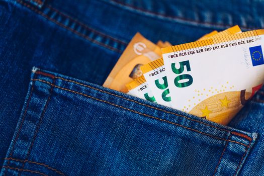 Euro bills in jeans pocket background. Euro banknotes in jeans back pocket. Concept of rich people, saving or spending money. Euro bills falling out. Easy to steal the money. Irresponsible action.