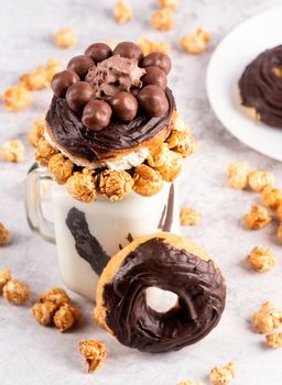 chocolate donut milkshake in a mason jar decorated with caramel popcorn, whipped cream and cocoa candies