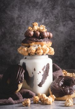 Ice cold chocolate donut milkshake in a mason jar decorated with caramel popcorn, whipped cream and cocoa candies, low key