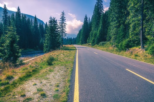 Mountain road. Landscape with rocks, sunny sky with clouds and beautiful asphalt road in the evening in summer. Vintage toning. Travel background. Highway in mountains. Transportation