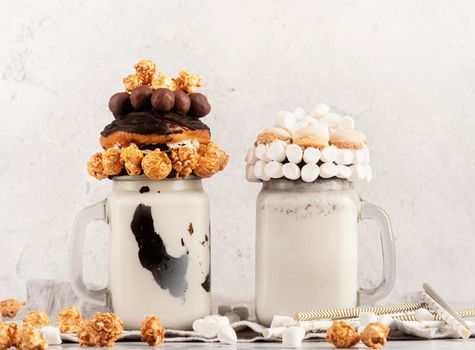 Milkshakes in mason jars decorated with whipped cream, popcorn, donuts, candies and marshmallows