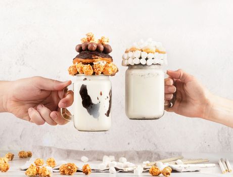 Friends drinking crazy milkshakes. Hands clanging glasses with freakshakes on a party