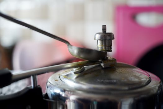 Pressure cooker in an indian kitchen with the whistle pressure release valve held open with a spoon. Shows a staple of indian kitchenware for cooking rice, potatoes and pulses