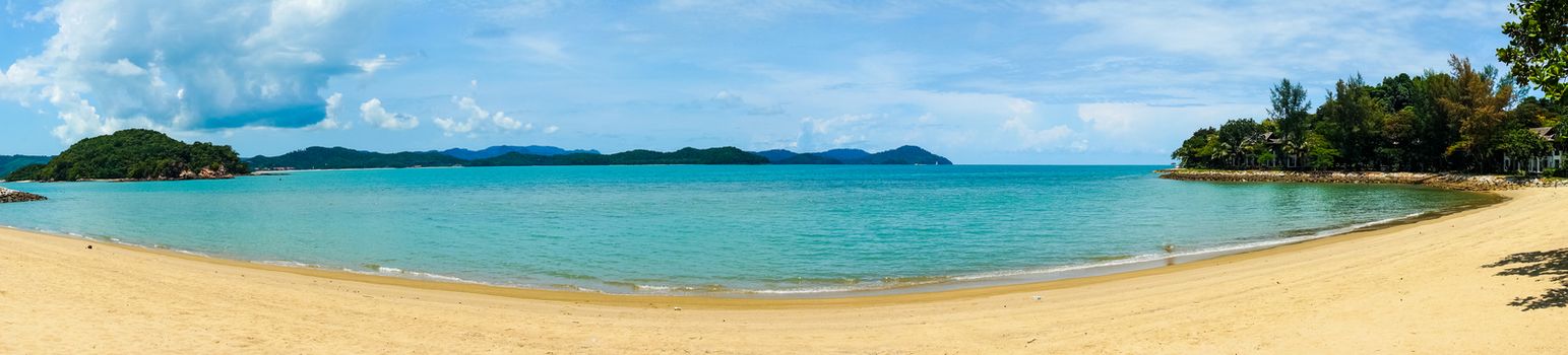 Panoramic shot of a beautiful golden sand beach with blue water beautiful fluffy clouds shot in Malaysia. Shows a perfect vacation spot to relax and unwind