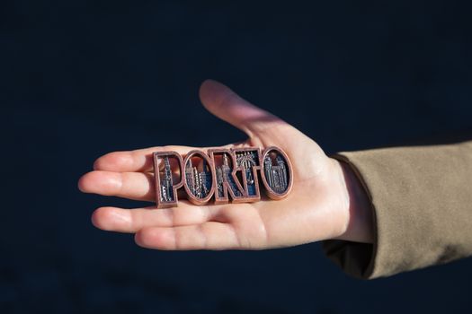 Women hand holding Porto magnet souvenir with Porto name in Portugal.
