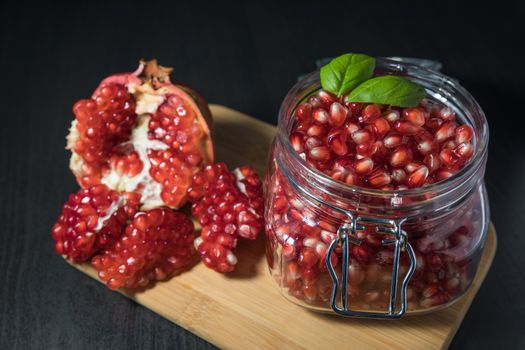 Delicious pomegranate seeds placed in glass jar with fresh organic pomegranates on rustic wooden background.Close up,Copy space