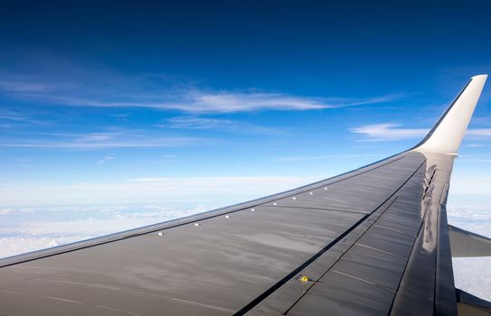 Wing of the plane on blue sky background. View of plane wing and sky from airplane window. Wing airplane over blue sky