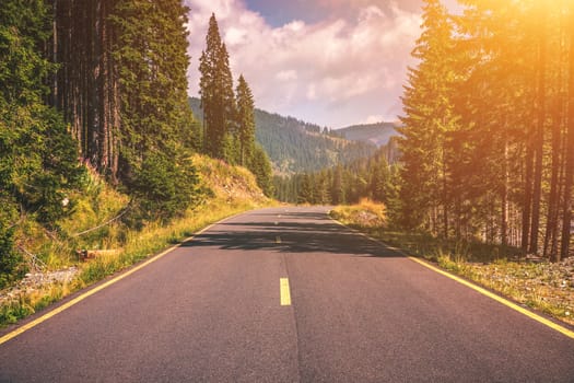 Mountain road. Landscape with rocks, sunny sky with clouds and beautiful asphalt road in the evening in summer. Vintage toning. Travel background. Highway in mountains. Transportation