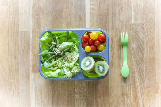 Collapsible silicon lunch box with food (green salads, tomatoes, kiwi) on wooden table