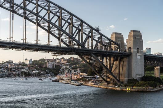 Sydney, Australia - February 12, 2019: Harbour bridge north side landing during sunset. Horizon is north shore of bay with Kirribilli neighborhood and Luna Park. Boats on water.