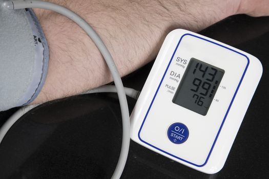 Man measuring his blood pressure at home with an automatic blood pressure monitor. Picture of the machine and arm of the person with results of the test on the screen