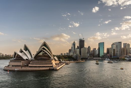 Sydney, Australia - February 12, 2019: North side of the Opera House and city skyline. Light Blue sky and gray water. Circular bay ferry terminal and railway station. Boats in water.