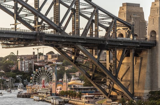 Sydney, Australia - February 12, 2019: closeup of Harbour bridge north side landing during sunset with Kirribilli neighborhood and Luna Park. Boats on water. Landscape.