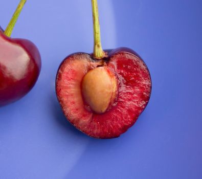 Close-up of halved ripe black cherry against blue.