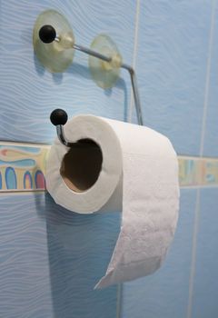 Toilet paper roll hanging over blue ceramic tiles.