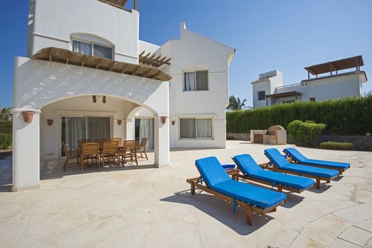 Luxury villa show home in tropical summer holiday resort with sun chairs on outdoor patio terrace area