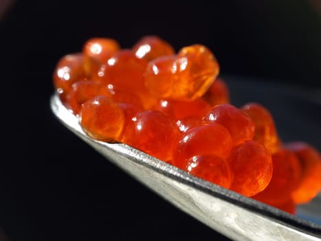 Red caviar on a spoon against black background