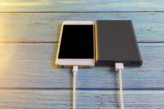 Close up smartphone charging with power bank on blue background with copy space. Smartphone charging with power bank by white USB cable.