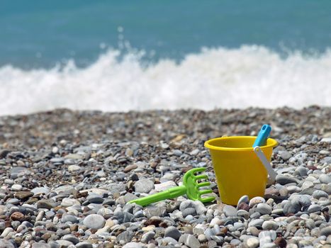 Yellow bucket and green rake on a beach.