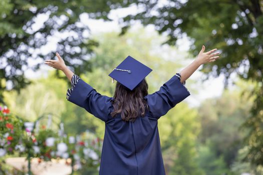 Back view of young woman graduating put her hands up and celebrating feeling so happy.