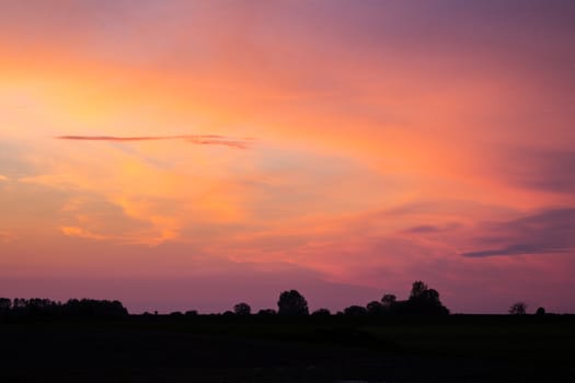 Natural Sunset Sunrise Over Field Or Meadow. Bright Dramatic Sky And Dark Ground. Countryside Landscape Under Scenic Colorful Sky At Sunset Dawn Sunrise. Sun Over Skyline, Horizon. Warm Colours.