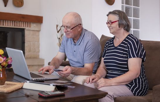 Senior couple shopping online on laptop using credit card at home. Internet banking at home concept. Focus on senior man face