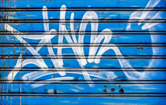Closed shutter covered with graffiti and blue background.