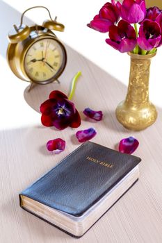 Holy Bible and old gold alarm clock with flowers on wooden table background. Time for studying, reading and spirituality concept.