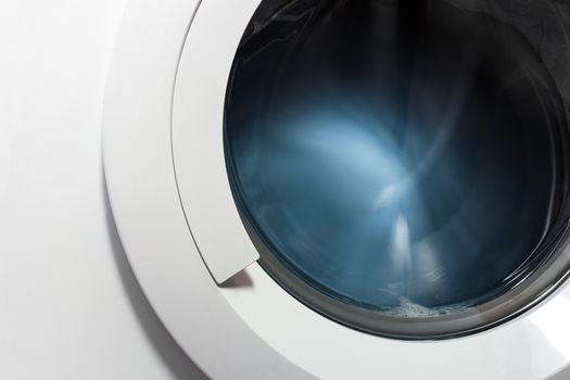 Front view and portion of the porthole of the washing machine during washing and rotation of the drum containing clothes blue