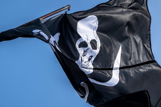 Pirate flag waving in wind against blue sky. Close up.