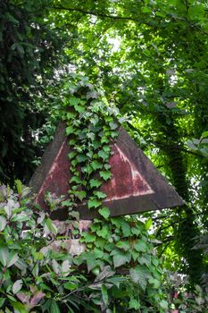 Road sign rusty and covered by the surrounding vegetation.