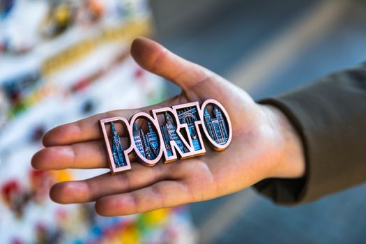 Women hand holding Porto magnet souvenir with Porto name in Portugal.