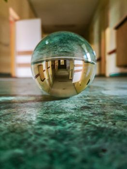 Long corridor with green covering on the floor reflected in crystal glassy lensball in old abandoned hospital