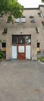 Vertical panoramic view of entrance to old abandoned hospital with glass barred doors