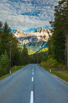 Dolomite Alps in Italy. Beautiful day. The road passes in the coniferous forests at the foot of limestone and dolomite rocks. The concept of active and car tourism