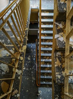 Top down view of concrete staircase with metal railings and peeled paintings from walls in old abandoned hospital