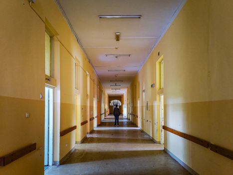 Man standing at center of corridor in old abandoned hospital
