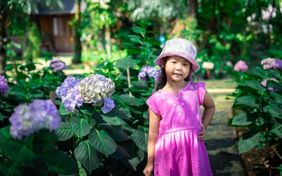 little asian girl in pink dress and hat standing in flower garden