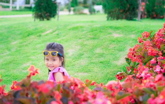 little asian girl in pink dress sitting on the ground in flower garden