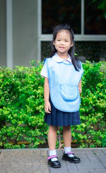 Portrait of happy little girl in Thai school uniform standing on footpath, ready back to school