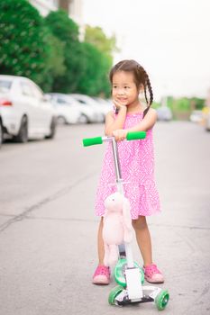 Portrait of little asian girl with scooter and doll on the street