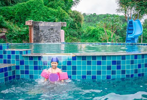 little asian girl wearing inflatable sleeves playing in the pool