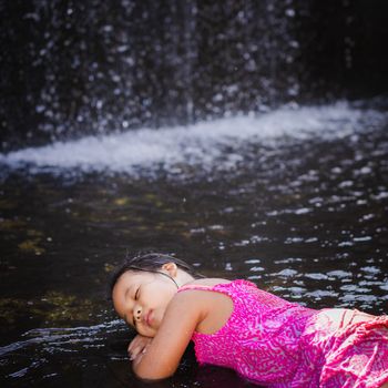 happy little asian girl sleeping near waterfall