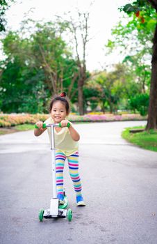 Cute little asian girl learning to ride a scooter in a park