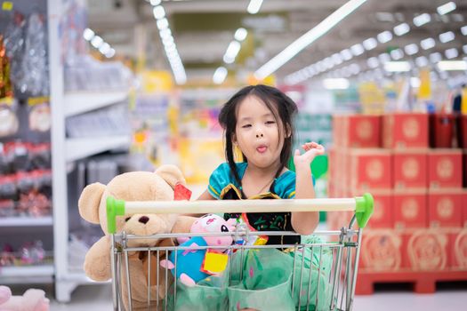 little asian girl in princess costume sitting with dolls in the cart between shopping